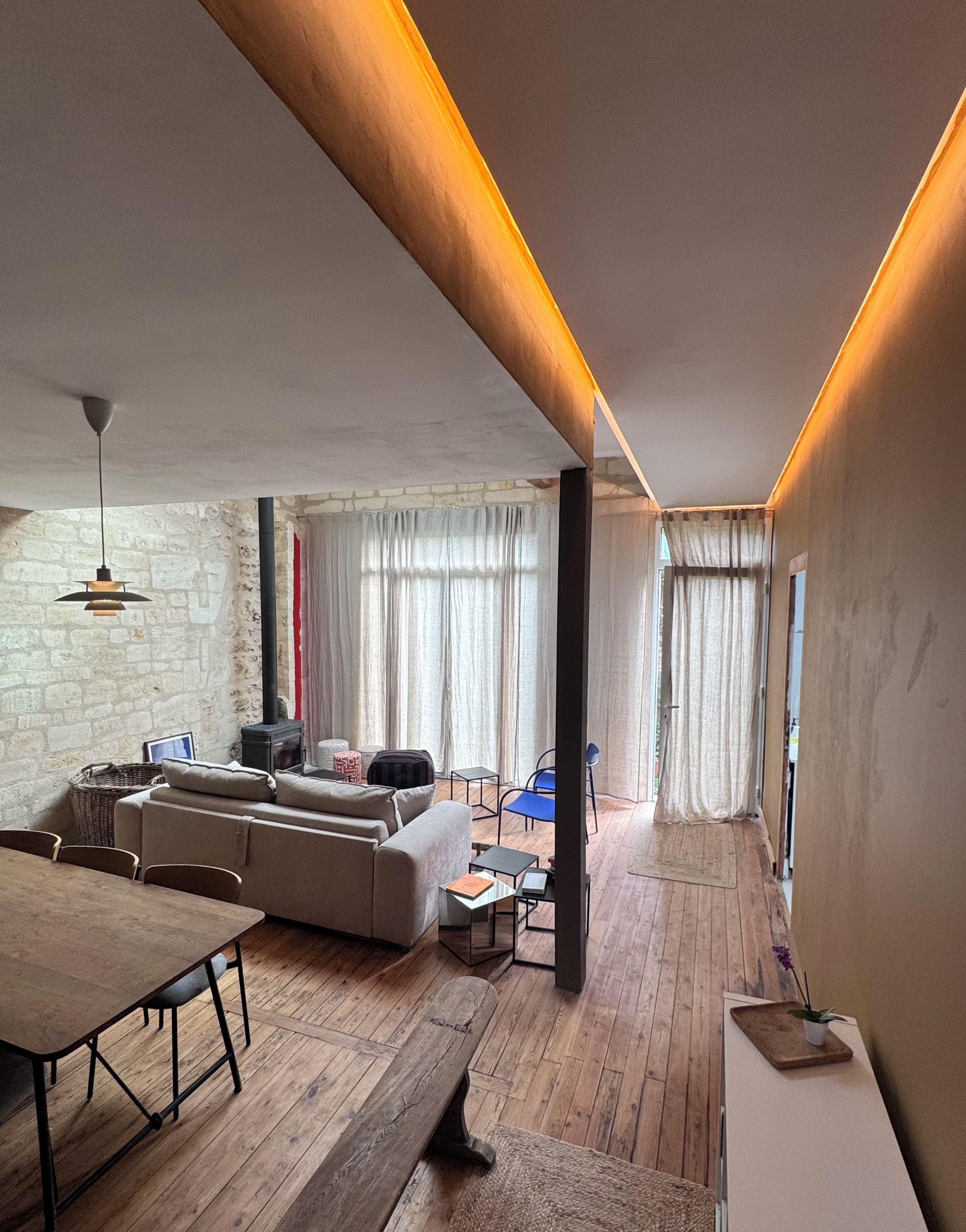 A modern living room with a sofa, dining table, and chairs. There is a fireplace and a window with curtains.