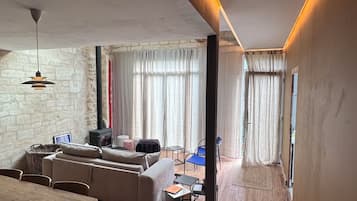 A modern living room with a sofa, dining table, and chairs. There is a fireplace and a window with curtains.