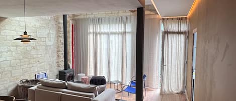 A modern living room with a sofa, dining table, and chairs. There is a fireplace and a window with curtains.
