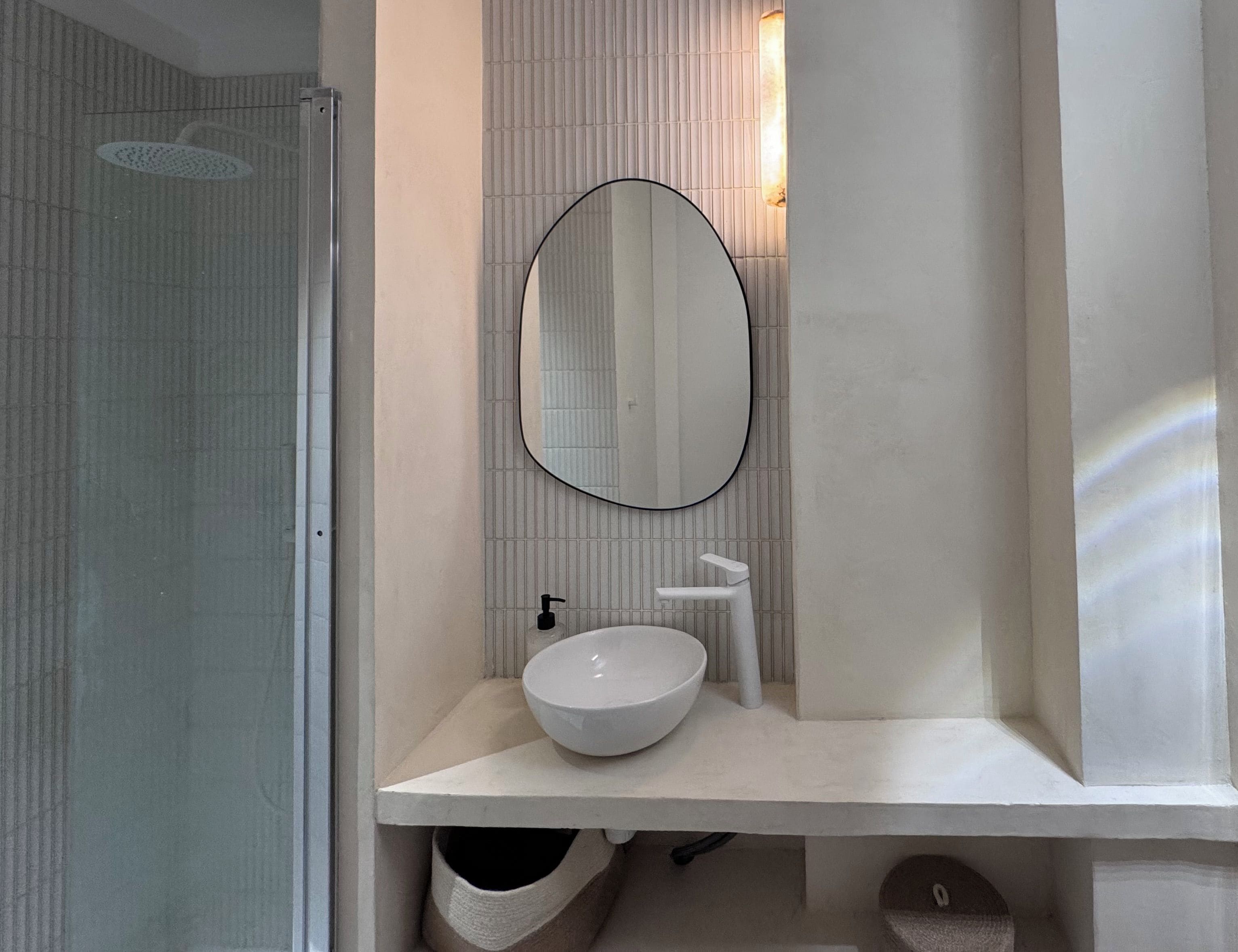 A modern bathroom with a white sink, a round mirror, and a shower area.