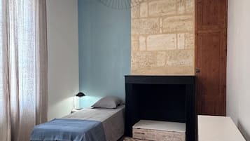 A bedroom with two beds, a hanging light fixture, a fireplace, and a wooden floor.