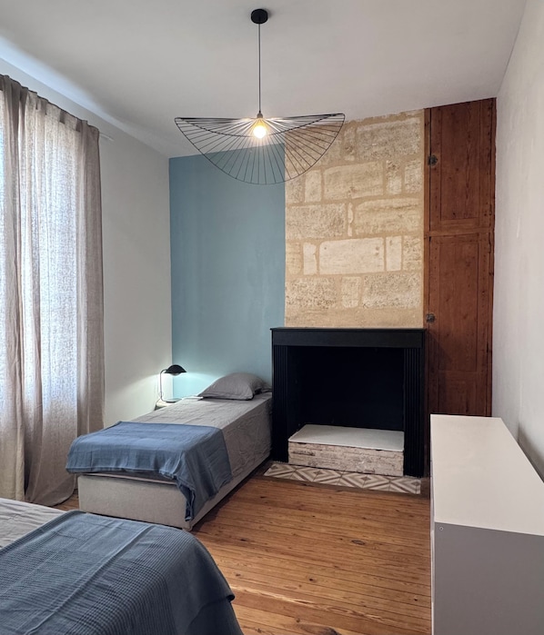A bedroom with two beds, a hanging light fixture, a fireplace, and a wooden floor. - Bordeaux-style townhouse with a garden, a 5-minute walk from the train station (Bordeaux)