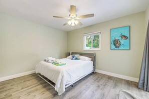 A bedroom with a bed, a ceiling fan, a window, and two wall art pieces. - The Saltwater House at Deerfield (Deerfield Beach)