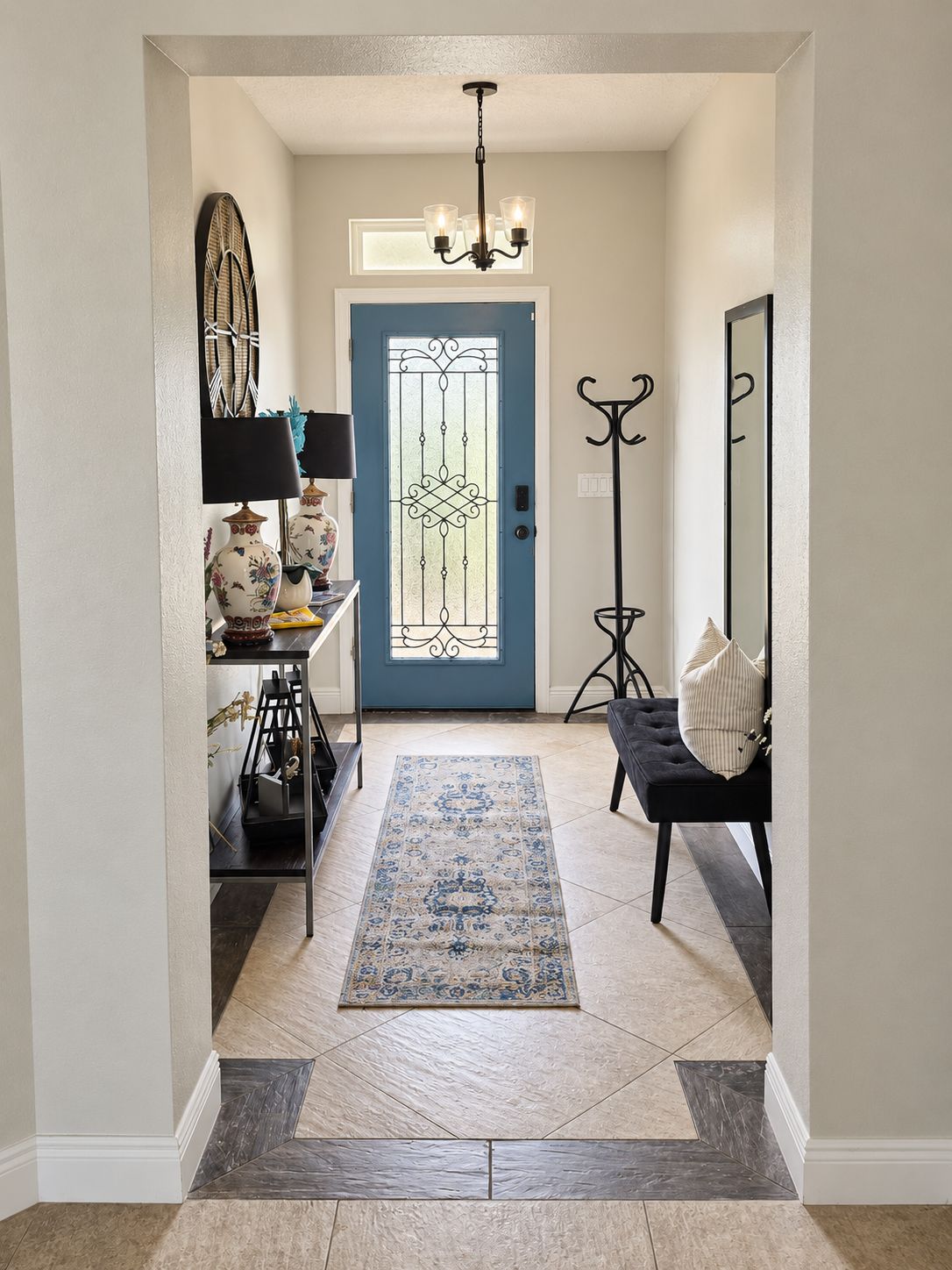 A hallway with a blue door, a black bench, a floor lamp, a table with decorative items, and a patterned rug.