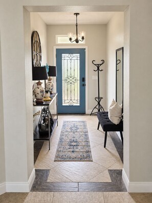 A hallway with a blue door, a black bench, a floor lamp, a table with decorative items, and a patterned rug. - A home away from home! A very spacious and comfortable place to relax! (Orlando)
