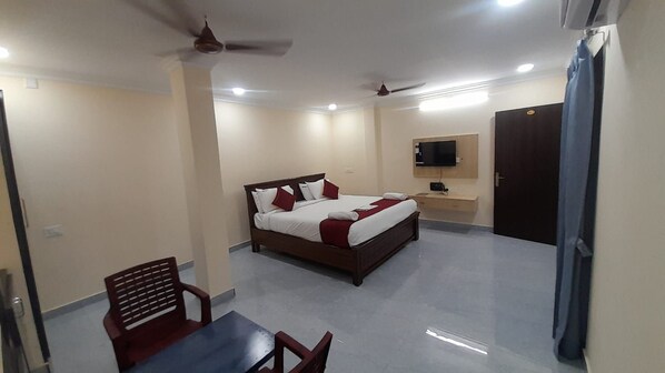 A hotel room with a bed, a desk, a chair, a TV, and a ceiling fan. - MMR RESIDENCY (Tirupati)