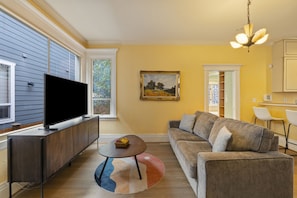 A living room with a flat-screen TV, a sofa, a coffee table, and a painting on the wall. - Victorian 3BR with Jetted Tub + Fireplaces - Central District (Seattle)