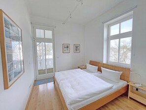 A bedroom with a large bed, two bedside tables, a radiator, and a window. - in the House on the Dune (Binz)