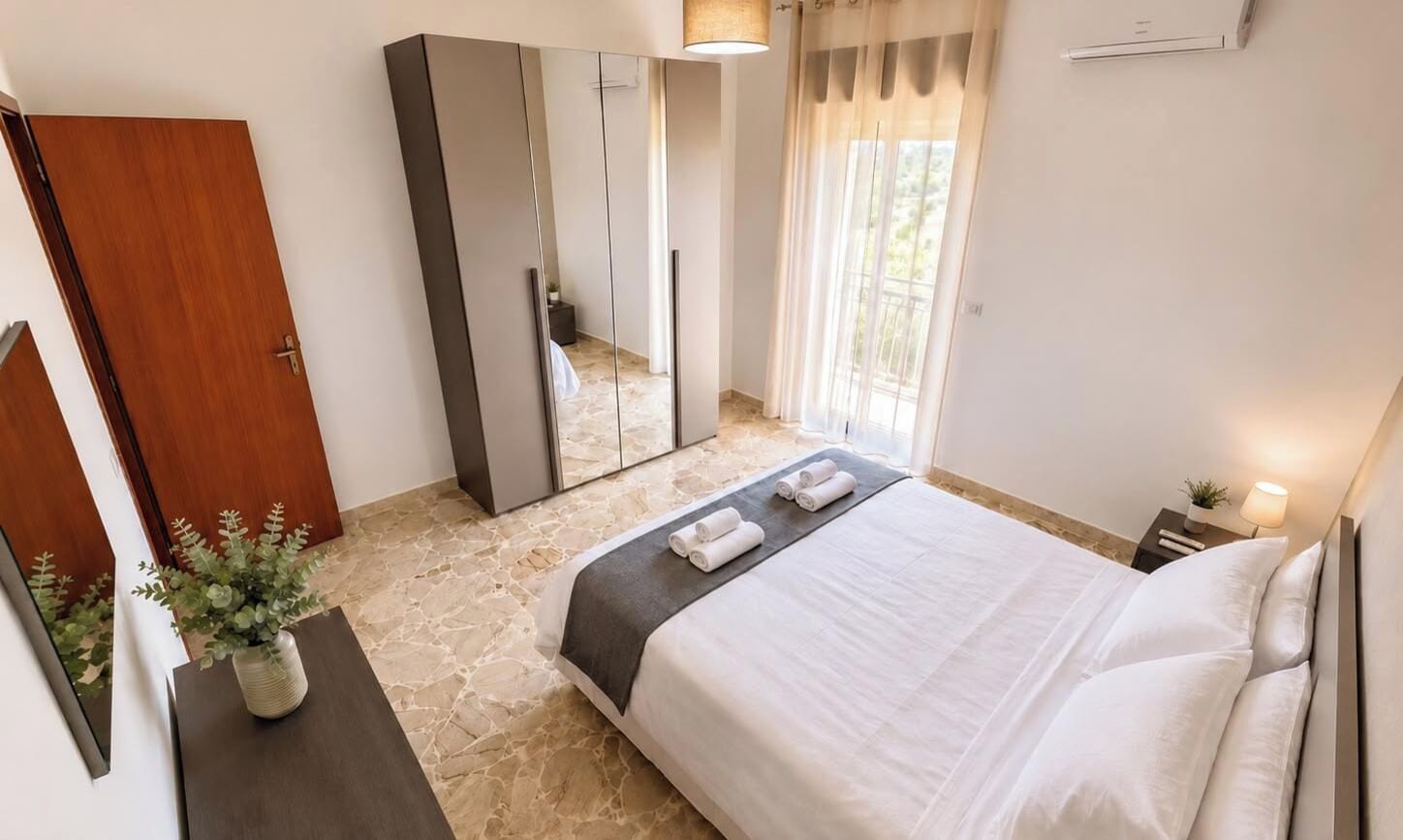 Une chambre d’hôtel avec un lit, une table de chevet, un miroir, une armoire et une plante en pot.