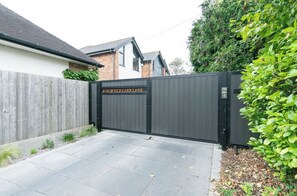 A gated driveway leading to a residential property with a brick house and a modern garage. - A Little Home of Your Own in Poulton — Gated Entrance & Parking (Poulton-le-Fylde)