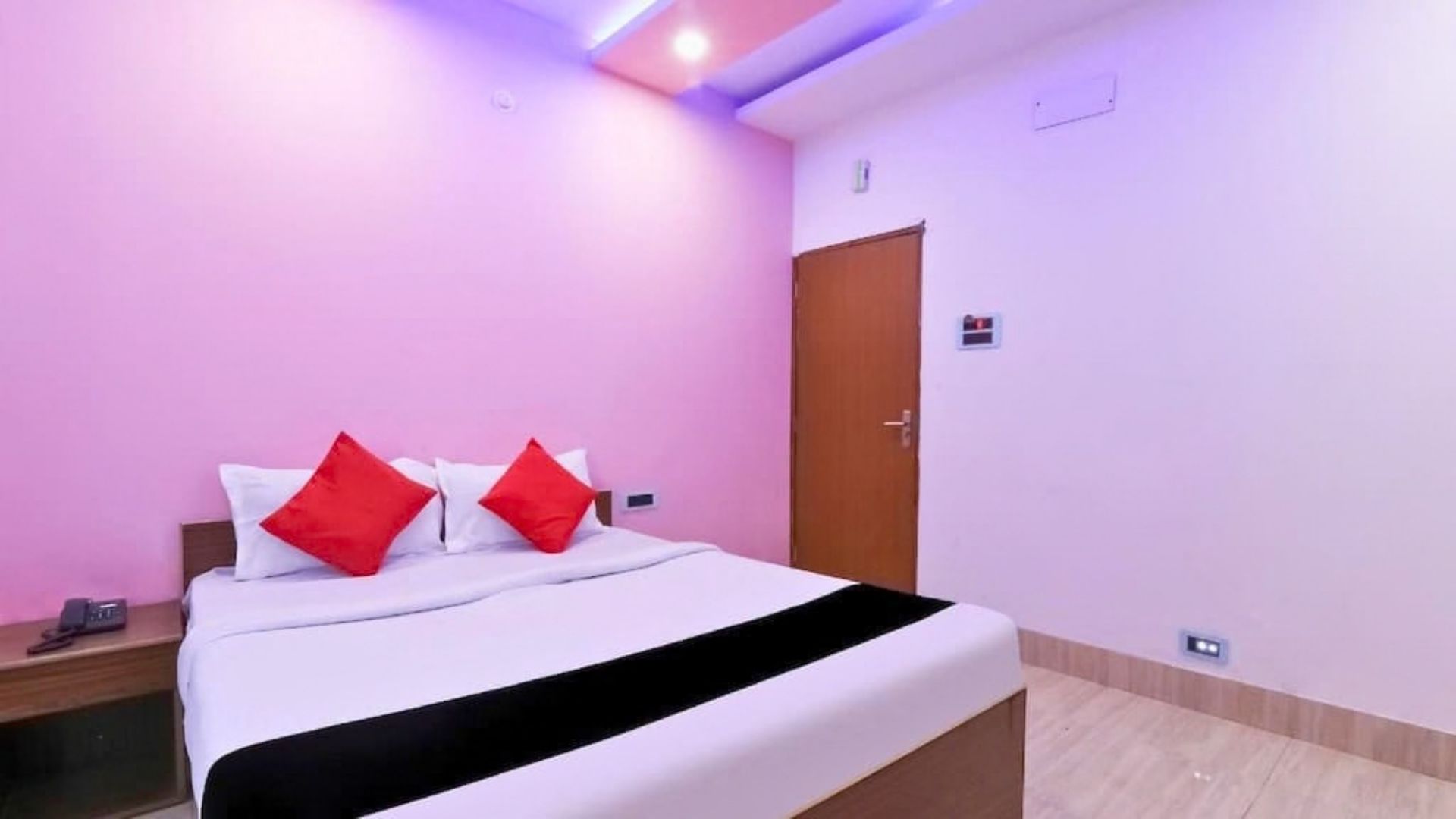 Une chambre d’hôtel avec un lit, une table de chevet, une porte et un luminaire fixé au mur.
