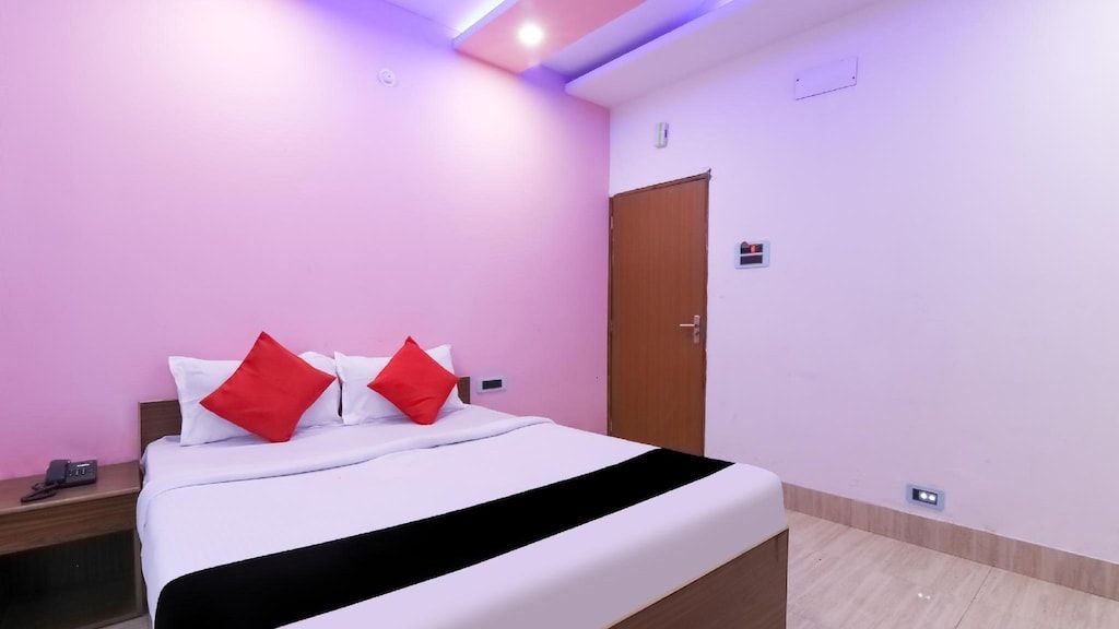 Quarto de hotel com cama, mesa de cabeceira, porta e interruptor de luz na parede.