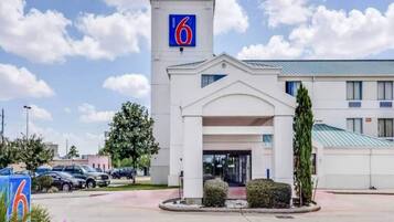 A motel with a prominent '6' sign, a central entrance, and a parking lot with several cars.