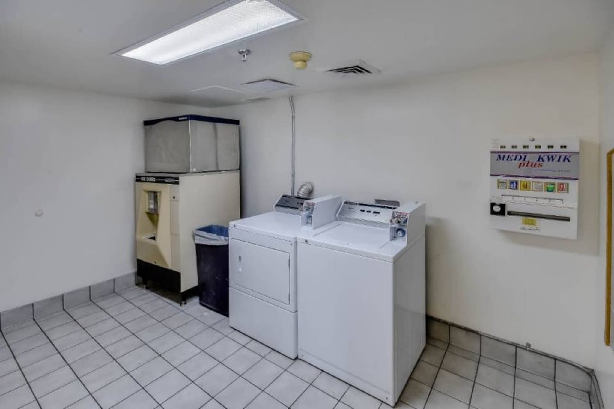 A laundry room with a washing machine, dryer, and a trash bin.