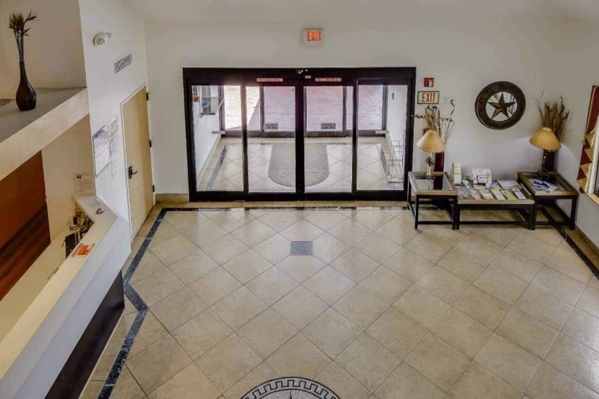 A hotel lobby with a reception desk, a seating area with a table and chairs, and a large glass door leading outside.
