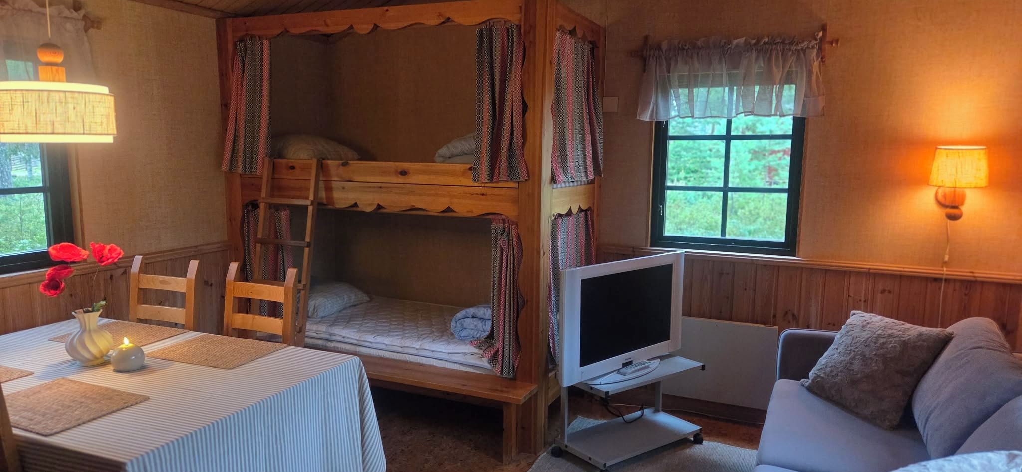 A bunk bed with a television on a stand, a table with a vase and candle, and a couch with pillows.