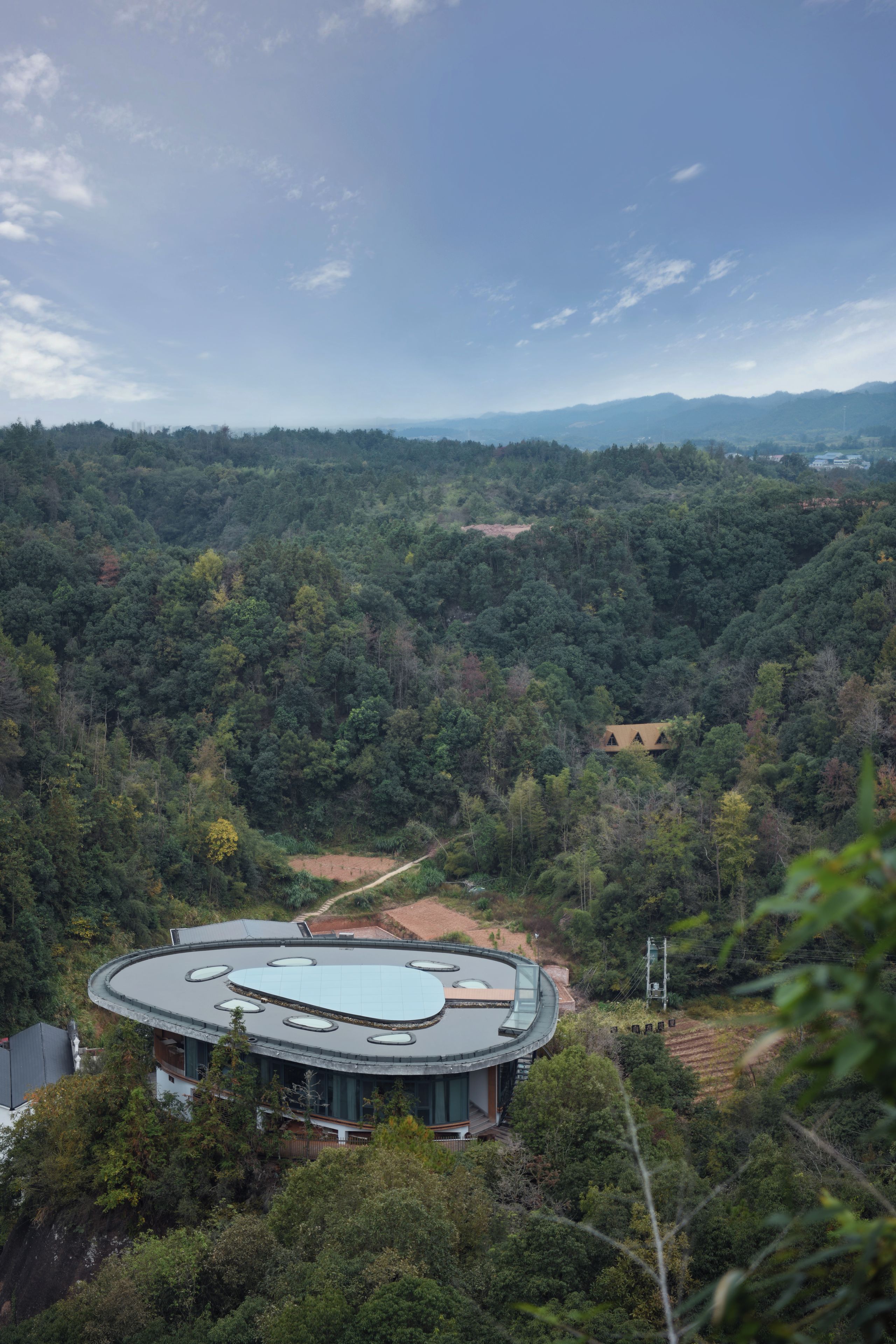 A circular building with a flat roof surrounded by dense forest.
