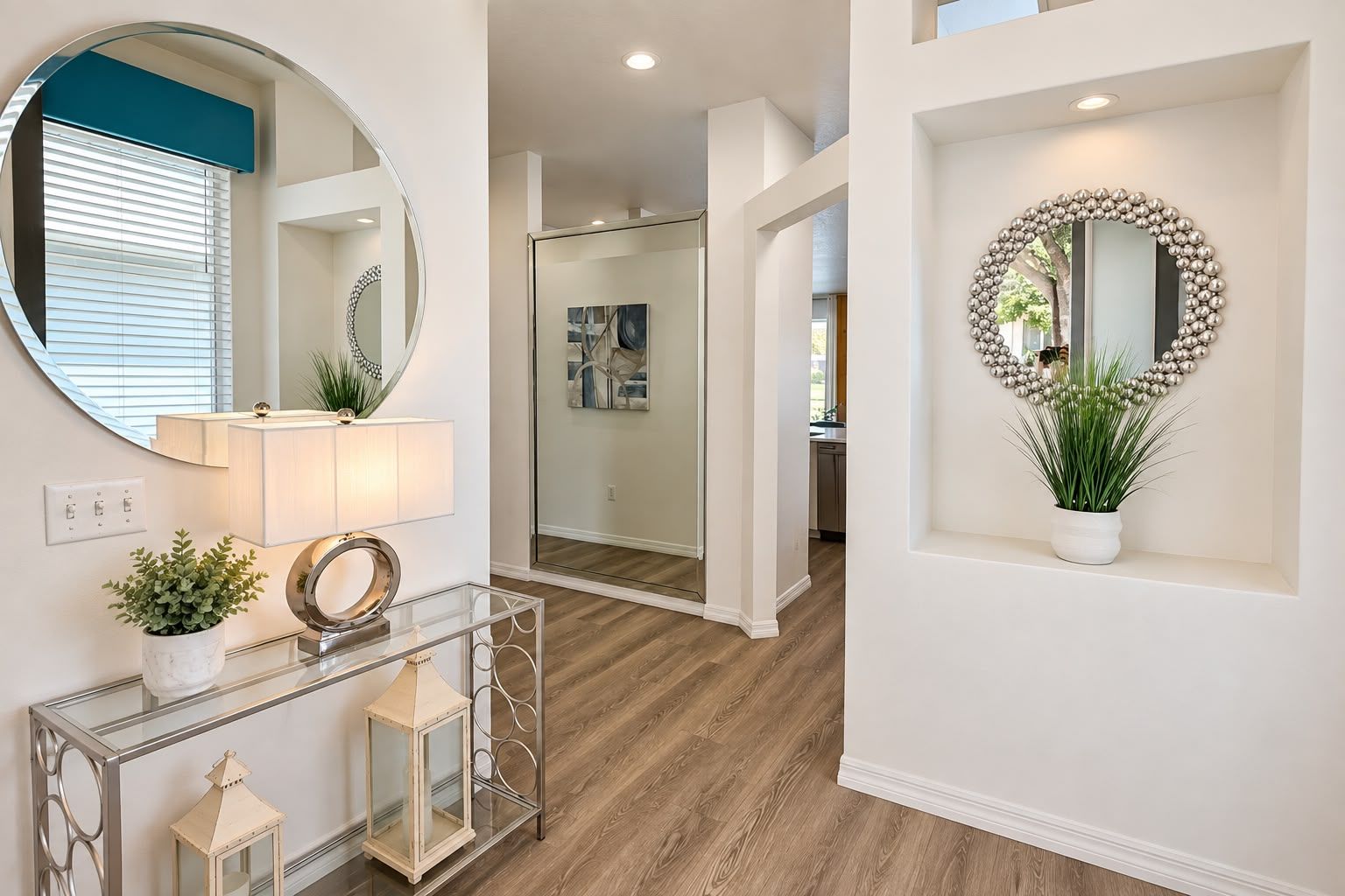 A hallway with a round mirror, a console table with a lamp, and a potted plant.