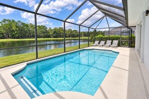 A swimming pool with a view of a lake and trees, surrounded by a covered area with lounge chairs. - Lakefront near Disney: Pool + LEGO game room (Kissimmee)