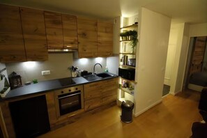 A modern kitchen with wooden cabinets, a black countertop, and a built-in oven. - Chamonix Gaillands (Chamonix-Mont-Blanc)