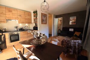 A modern kitchen with wooden cabinets, a dining area with a table and chairs, and a living room with a sofa and a dog. - Chamonix Gaillands (Chamonix-Mont-Blanc)