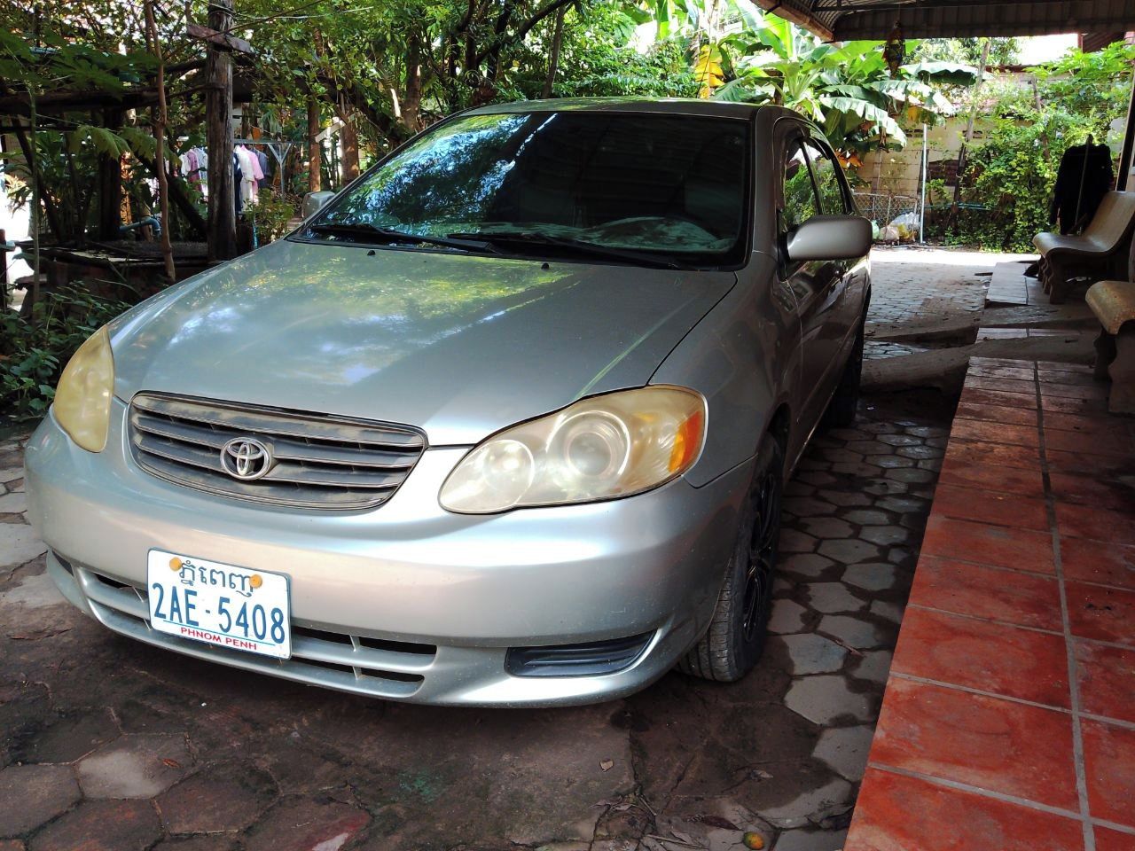 A silver car parked in a covered outdoor area with a tiled floor.