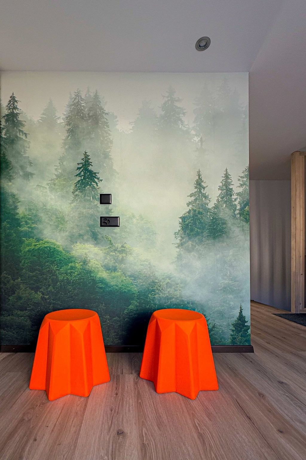 A room with a forest mural on the wall, two orange tables, and a wooden floor.