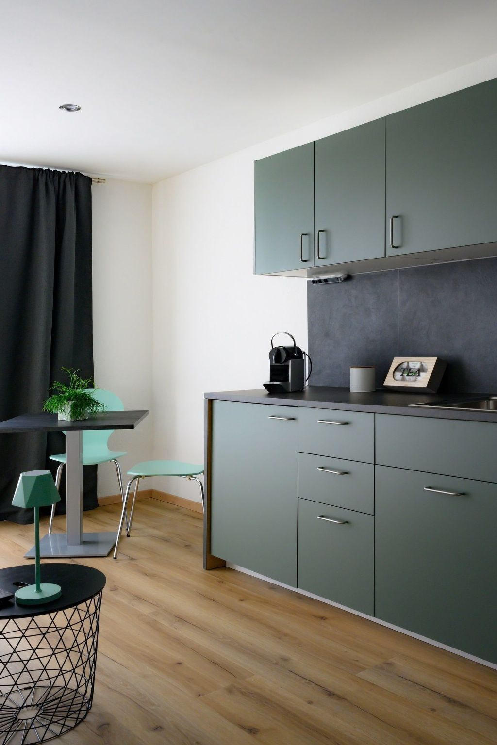 A modern kitchen with grey cabinets, a black countertop, and a small dining area with a table and chairs.