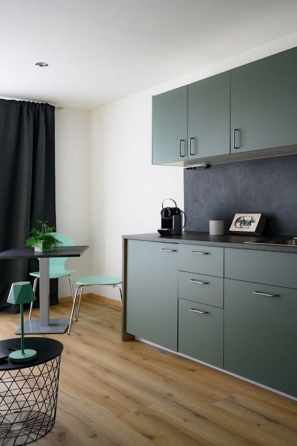 Une cuisine moderne avec des meubles gris, un plan de travail noir et un petit coin repas comprenant une table et des chaises.