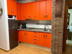 Una cucina con mobili arancioni, un frigorifero in acciaio inossidabile e uno schienale piastrellato.