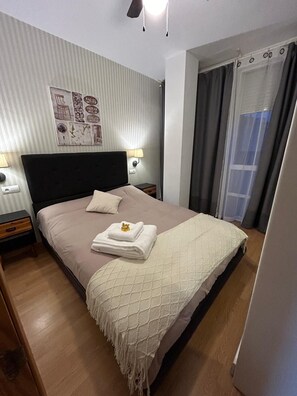 Ein ordentlich bezogenes Bett mit Kopfteil, ein Nachttisch mit Lampe und eine Wand mit einem gerahmten Bild.