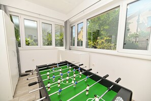 Ett rum med ett fotbollsspel, stora fönster och utsikt över grönområden utanför.