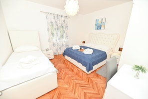A hotel room with two beds, a wooden herringbone floor, a white headboard, a nightstand with a lamp, and a small plant on a table. - Holiday home Lucia 5 minutes’ walk from Old Town in Trogir with private pool (Trogir)