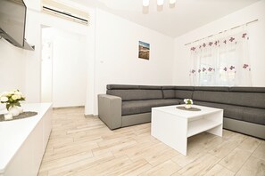 A modern living room with a grey sectional sofa, a white coffee table, and a wooden herringbone floor. - Holiday home Lucia 5 minutes’ walk from Old Town in Trogir with private pool (Trogir)