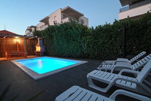 A swimming pool with lounge chairs, a wooden deck, and a hedge. - Holiday home Lucia 5 minutes’ walk from Old Town in Trogir with private pool (Trogir)