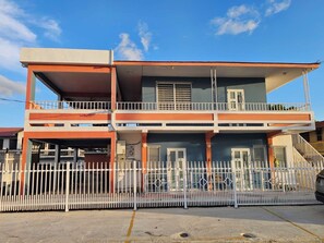 A two-story building with a balcony on the upper floor, a white fence in front, and a clear sky. - Casa Iliria 2: cozy 1-bedroom apartment with AC in charming Boquerón (Boquerón)