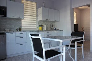 A modern kitchen with white cabinetry, a granite countertop, and a dining area with white chairs. - Casa Iliria 2: cozy 1-bedroom apartment with AC in charming Boquerón (Boquerón)