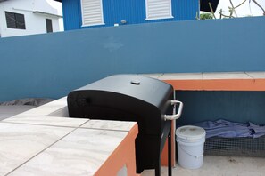 A barbecue grill on a tiled patio with a blue wall and a white bucket nearby. - Casa Iliria 2: cozy 1-bedroom apartment with AC in charming Boquerón (Boquerón)