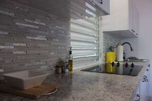 Une cuisine au design moderne, dotée d’un plan de travail en granit, d’un four encastré et d’une fenêtre avec des stores.