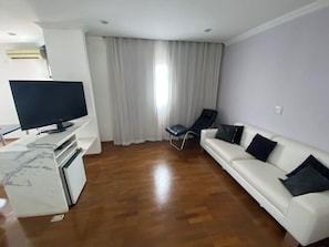 A living room with a flat-screen TV, a white sofa, a black chair, and a wooden floor. - Quality Hotel Sao Carlos (São Carlos)