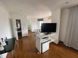 Una habitación con un televisor de pantalla plana sobre un soporte blanco, un mueble blanco pequeño y una mesa negra con objetos decorativos.
