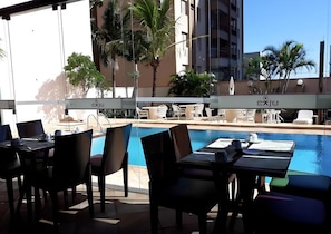 An outdoor pool area with lounge chairs and tables, surrounded by palm trees and a building in the background. - Quality Hotel Sao Carlos (São Carlos)