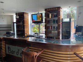 Zona de bar con un letrero que dice 'Bar d'o', estantes con vasos, una pantalla de televisión y vistas al exterior con vegetación.