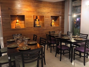 A dining area with wooden walls, multiple tables set for four, and three illuminated Buddha statues. - Quality Hotel Sao Carlos (São Carlos)