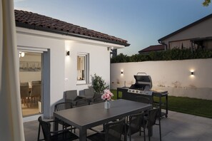 An outdoor patio with a dining table and chairs, a grill, and a view of a house with a tiled roof. - Casa Zucchero (Cukrići)