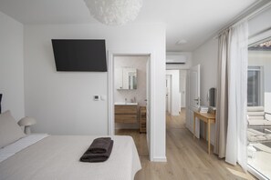 A modern bedroom with a bed, a flat-screen TV, a bedside table, and a view of the bathroom and balcony. - Casa Zucchero (Cukrići)