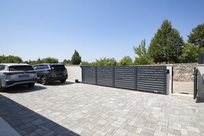 A parking area with two cars, a stone wall, and a metal gate. - Casa Zucchero (Cukrići)