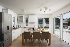 Een moderne keuken met witte kasten, een eettafel met stoelen en een uitzicht op de omgeving door grote ramen.