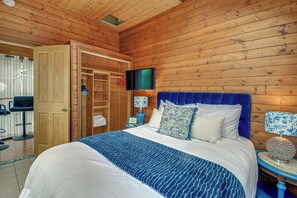 A wooden-paneled room with a bed, a television mounted on the wall, and a blue upholstered headboard. - 4-Unit Group Retreat! 2 Hot Tubs & Walk to Beach (Hansville)