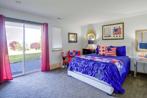 A bedroom with a large bed, a desk, a chair, a window with curtains, and a view of the outdoors. - 4-Unit Group Retreat! 2 Hot Tubs & Walk to Beach (Hansville)